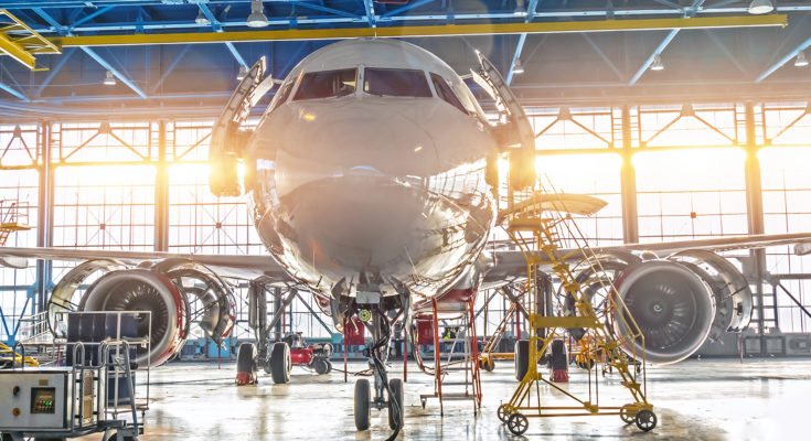 Civil airplane jet on maintenance of engine and fuselage check repair in airport hangar. Bright light at the gate